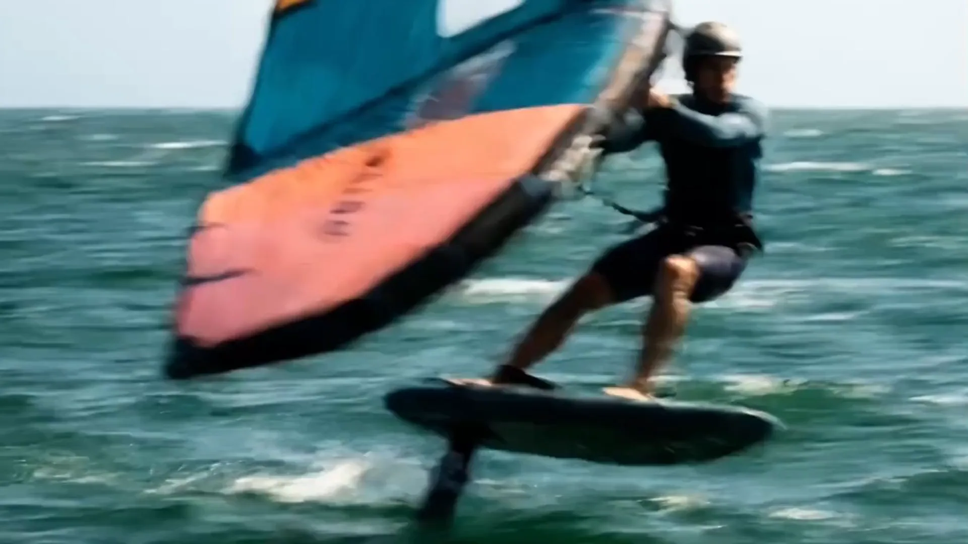 Wing-foiler em pleno voo sobre o mar, foil acima da água.